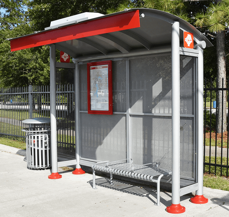 A signa sunset bus shelter is seen from the right side with a trash receptacle on the outside left, a rider information display on the inside left and a bench for three on the inside right.