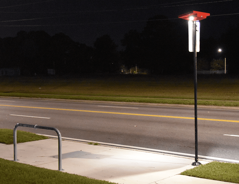 A bus stop is seen at night with a bus stop post with a light on top.