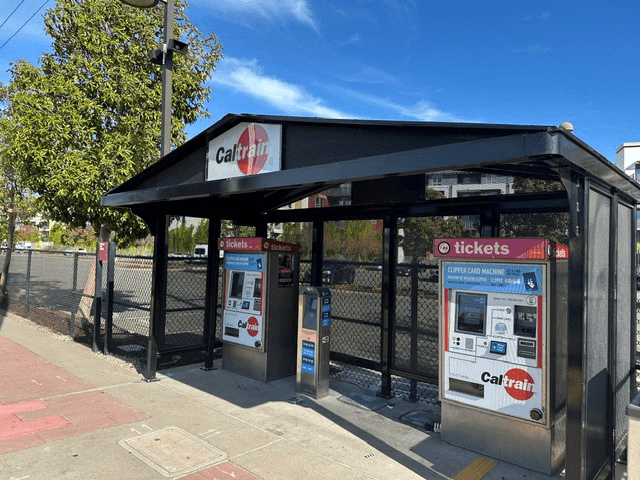 A CalTrain bus shelter is seen with ticket kiosks on either side of the inside of the shelter.