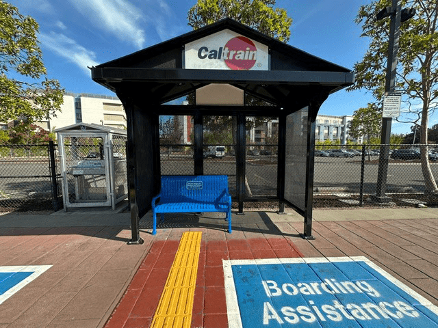 A Caltrain bus shelter is seen from the front with bench seating for two and a section reserved for boarding assistance on the right.