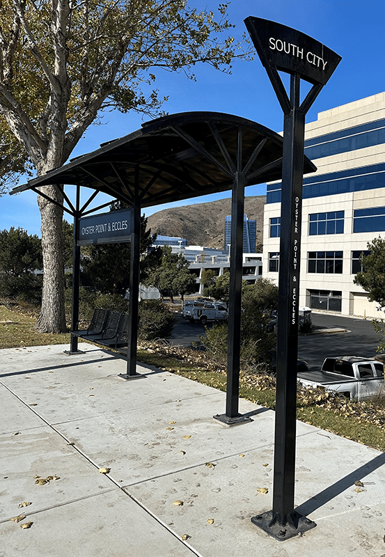 A bus shelter is seen from the front right with a bus stop post with signage reading South City on top.