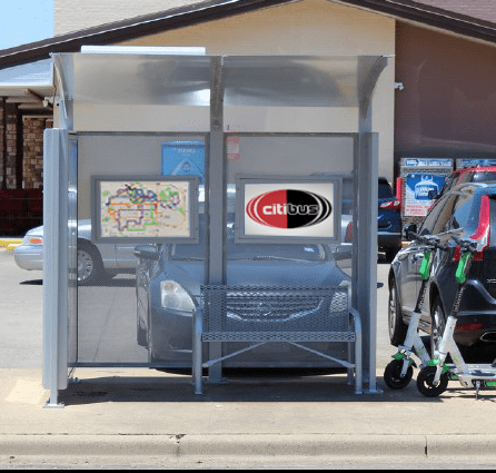 A siga custom bus shelter is seen from the front with two interior advertising/rider information displays and a single bench.