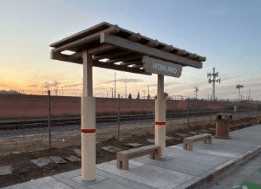 A bus shelter is seen at dusk with a bench under the shelter and a bench outside the right side of the shelter with signage that reads Highland.