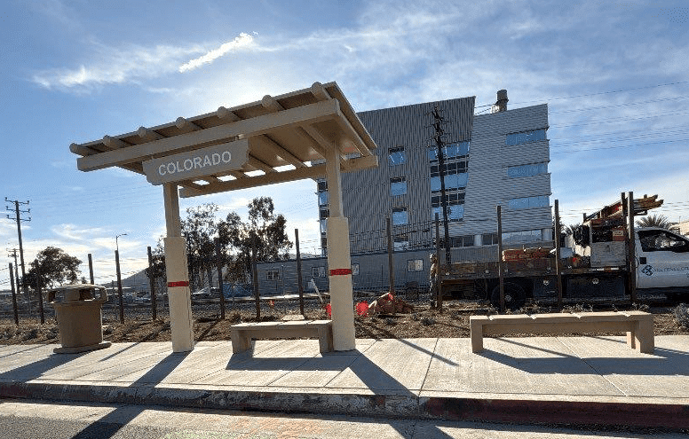 A signa custom bus shelter is seen from the front left with two benches, a trash receptacle and signage reading Colorado.