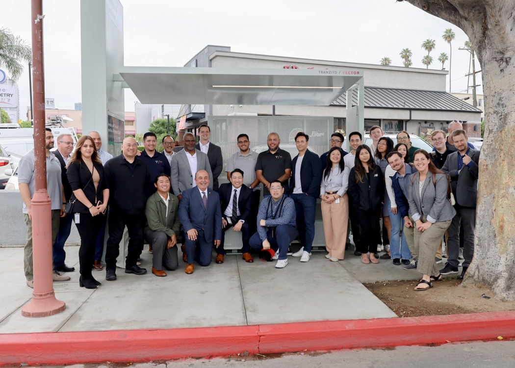 Partners and city leaders are gathered outside a bus shelter in Koreatown.
