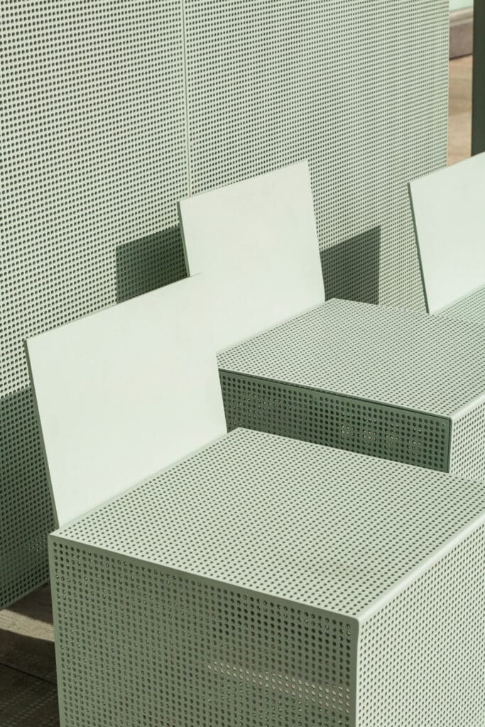 Modern la bus shelter seats are seen with square designs with round holes on a cream metal.
