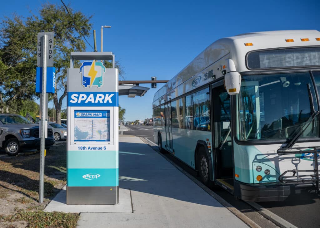 The side of a Spark bus shelter with the transit map on the side panel and a bus pulled up along the curb.